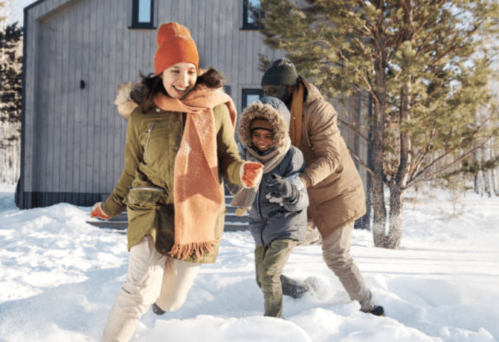 how to plan a family winter vacation on a budget - featured image featuring parents playing with kids outside in the snow